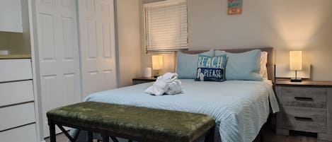 A bedroom with a bed, a bench, a nightstand, a lamp, and a door.