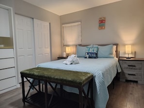 Een slaapkamer met een bed, een bankje, een nachtkastje, een lamp en een deur.
