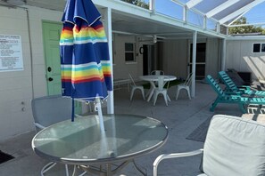 A covered outdoor area with a glass table, chairs, and a striped umbrella. - AMI Coastal Retreat Heated Pool 4BR 2BA Sleep 12 (Bradenton)