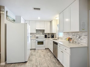 A modern kitchen with white cabinets, a built-in oven, a dishwasher, and a tiled backsplash. - AMI Coastal Retreat Heated Pool 4BR 2BA Sleep 12 (Bradenton)