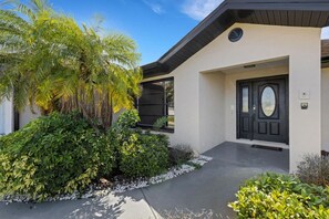 A modern building with a black door, a small porch, and lush greenery.
