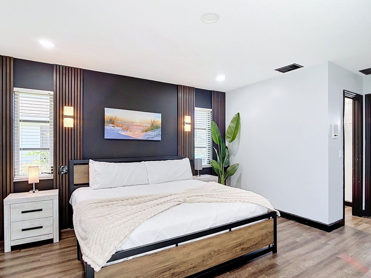 A modern bedroom with a bed, bedside tables, a wall-mounted TV, and a large window with blinds.