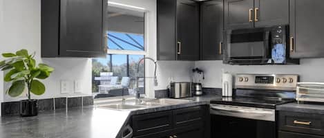 A modern kitchen with dark cabinetry, stainless steel appliances, and a large window providing natural light.