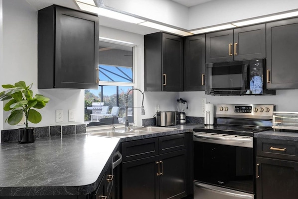 A modern kitchen with dark cabinetry, stainless steel appliances, and a large window providing natural light.
