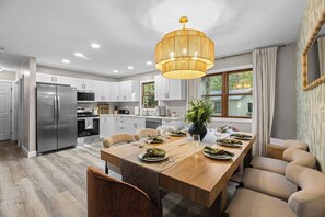 A modern kitchen with white cabinets, a stainless steel refrigerator, and a dining area with a wooden table set for four. - Sleeps 12, Hot Tub, Game room, Sauna, Theater (Logan)
