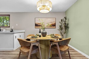 A dining area with a round table, chairs, a vase with flowers, a wine bottle, and a painting on the wall. - Sleeps 12, Hot Tub, Game room, Sauna, Theater (Logan)