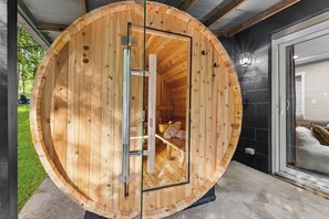 A wooden sauna with a glass door, a bench inside, and a black wall adjacent to it. - Sleeps 12, Hot Tub, Game room, Sauna, Theater (Logan)