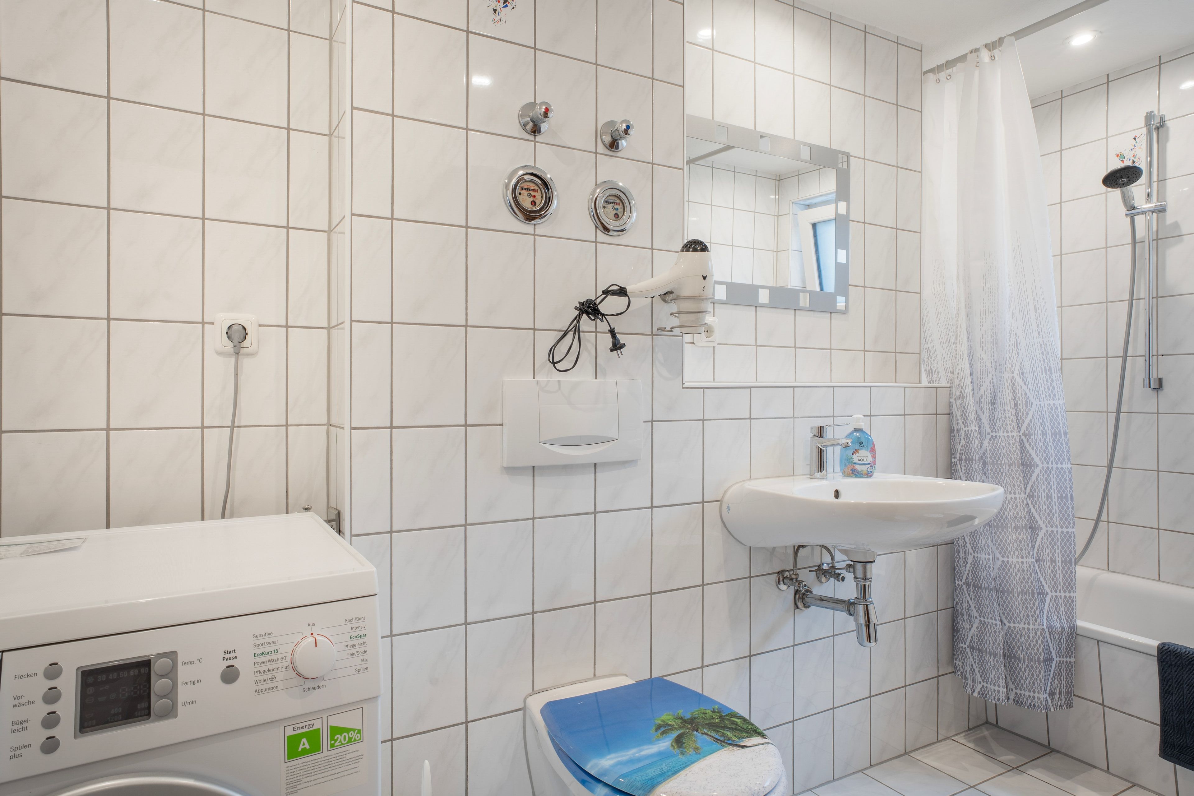 Een moderne badkamer met een witte betegelde muur, een inbouwspoelbak, een douche met glazen deur en een toilet met een tropisch design.