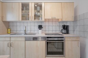 A modern kitchen with wooden cabinets, a dishwasher, an oven, a coffee maker, and a glass cabinet with dishes.