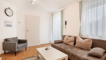 Een moderne woonkamer met een bank, een salontafel, een grijze fauteuil, een wandklok en een bordje met het WiFi-wachtwoord.