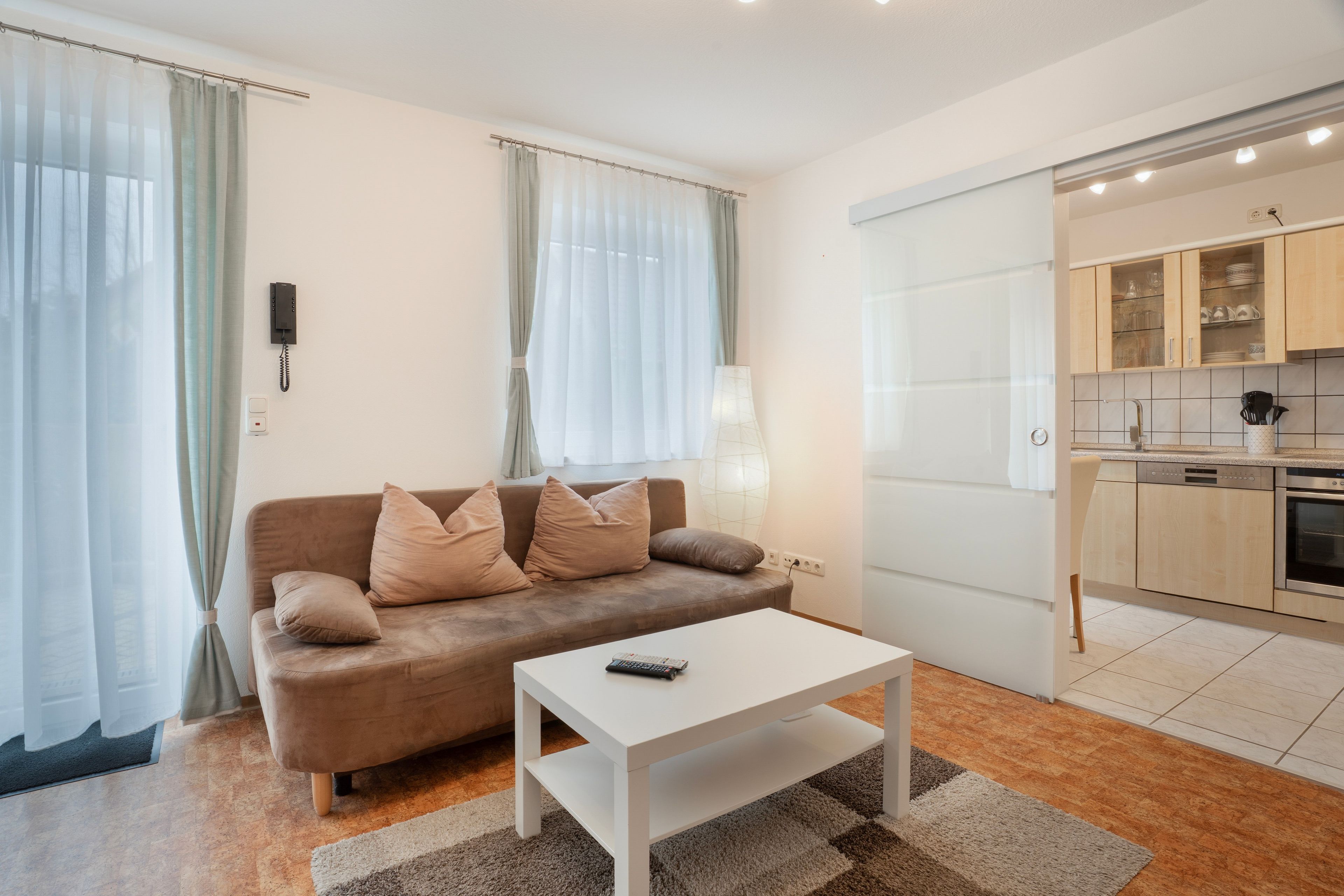 A modern living room with a sofa, a coffee table, and a kitchen area with cabinets and appliances.
