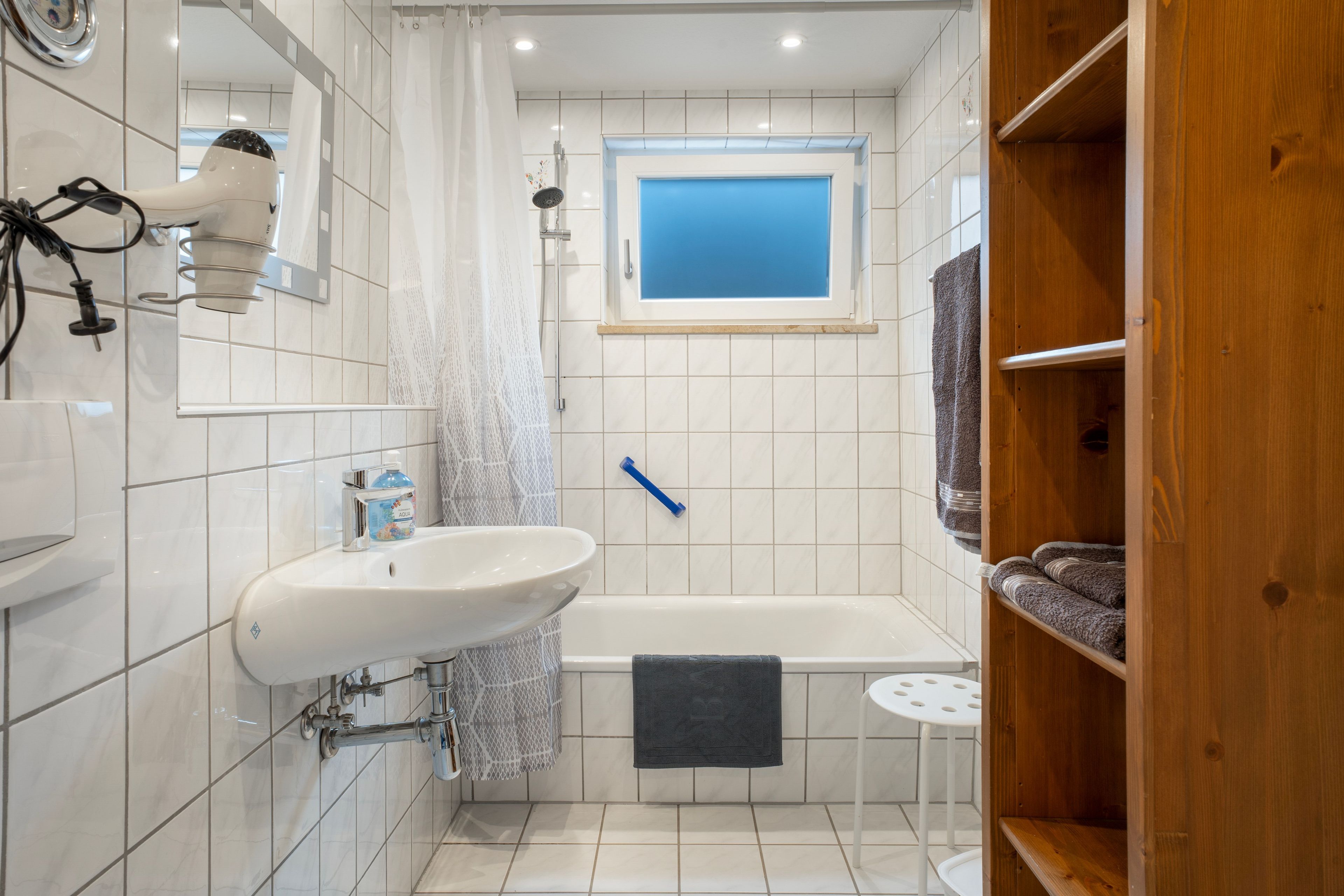 Un baño con un lavamanos blanco, una bañera, un perchero para toallas y una ventana.