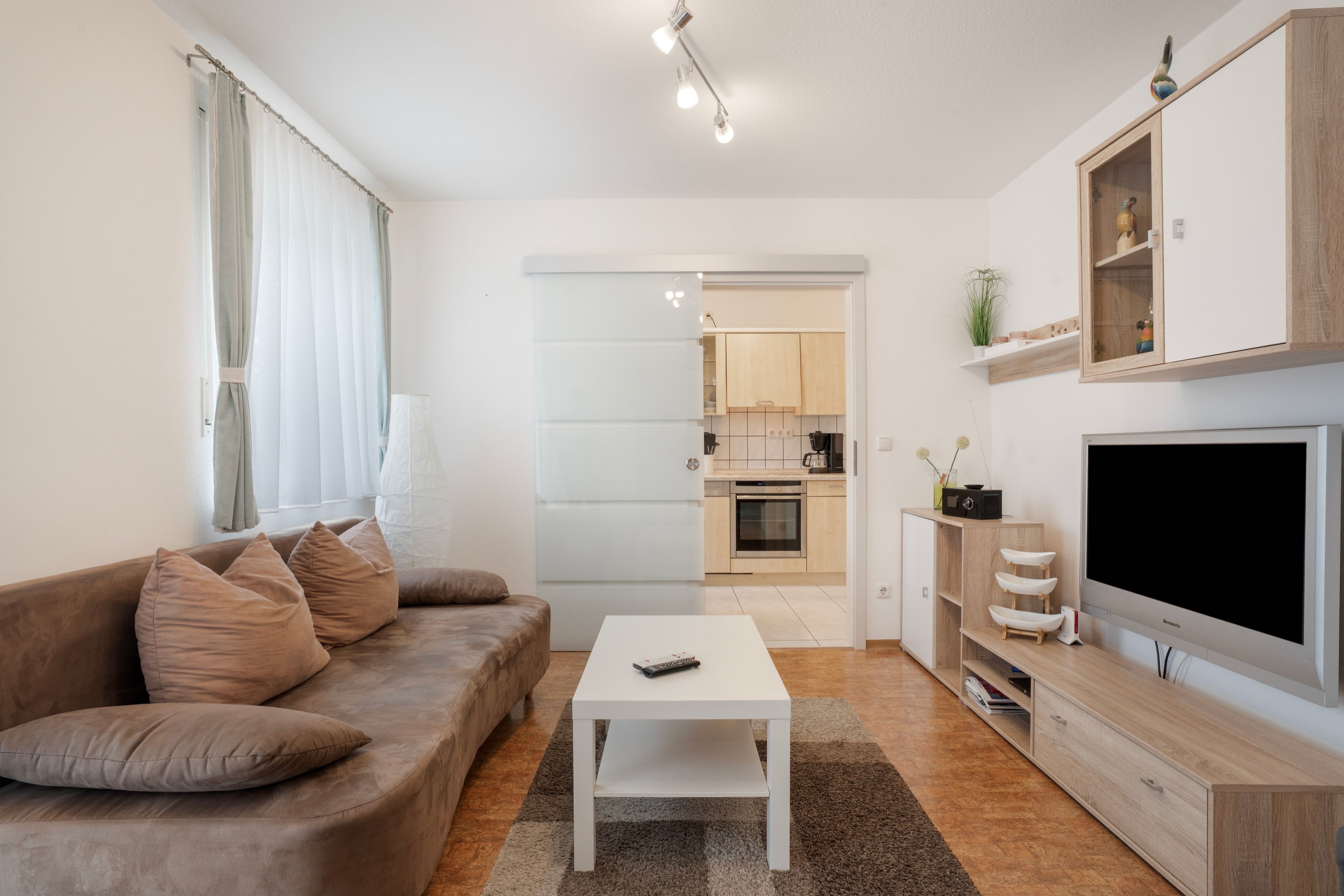 Un salon moderne avec un canapé, une table basse, un téléviseur et une cuisine en arrière-plan.