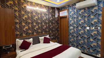 Una habitación de hotel con una cama, ventilador de techo, equipo de aire acondicionado y papel tapiz estampado.