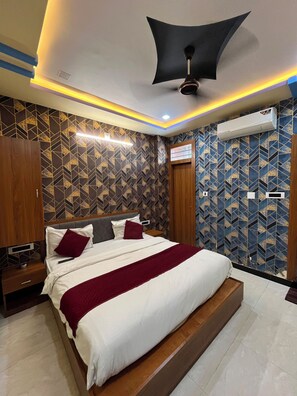 A hotel room with a bed, a ceiling fan, an air conditioning unit, and patterned wallpaper. - The Aravali hills  (Udaipur)