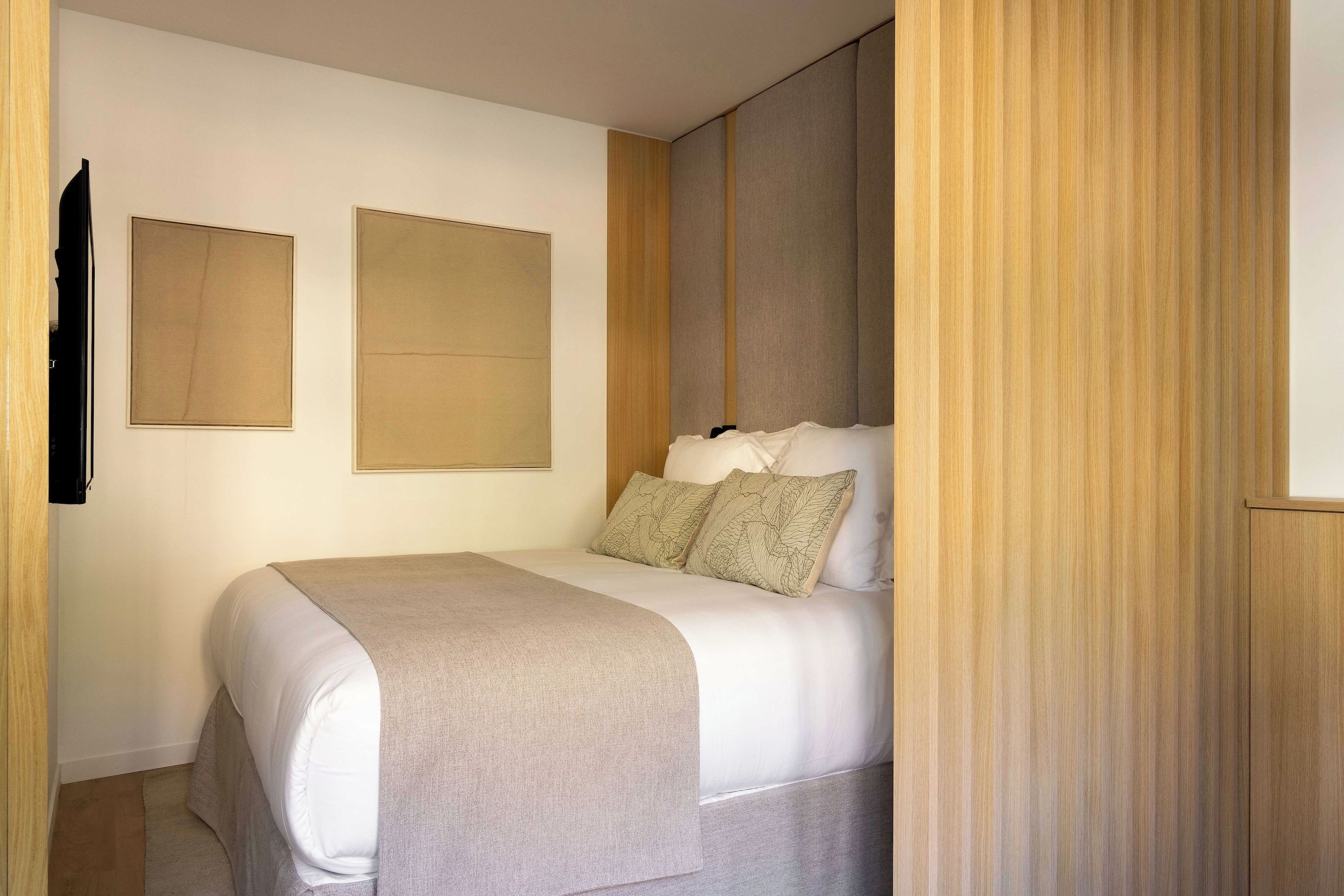 A bedroom with a bed, a wooden wardrobe, and two framed pictures on the wall.