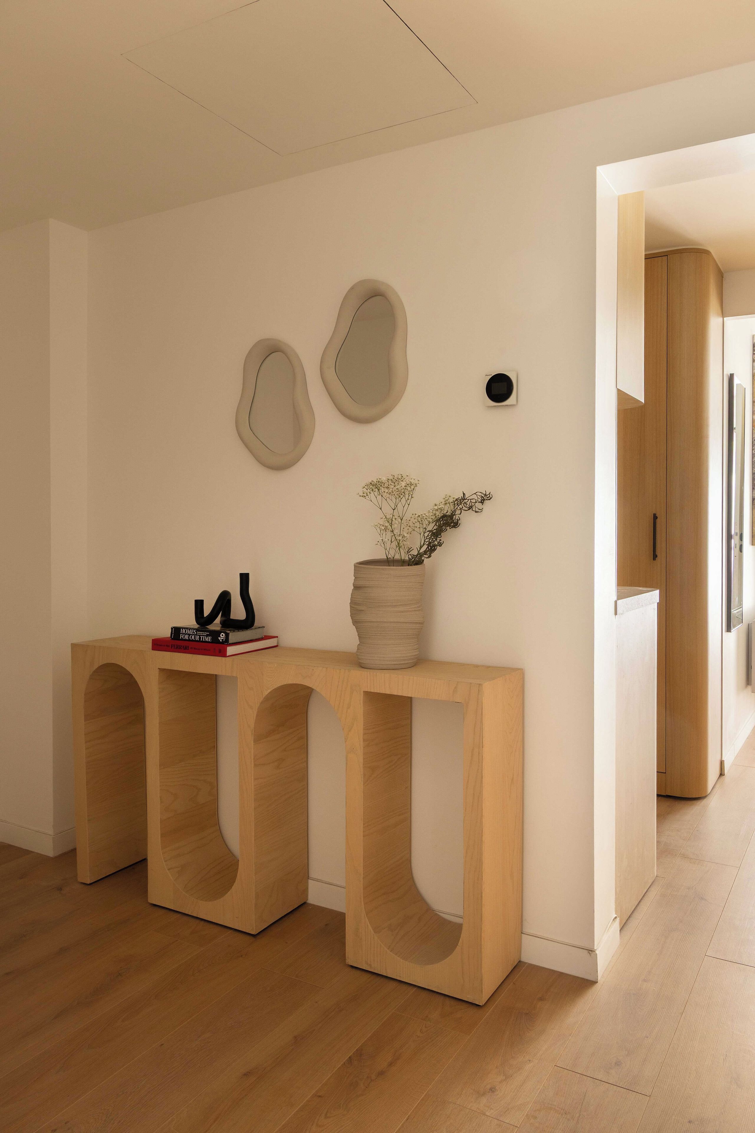 Un intérieur moderne avec une console en bois, un vase de fleurs et des œuvres d’art abstraites accrochées au mur.