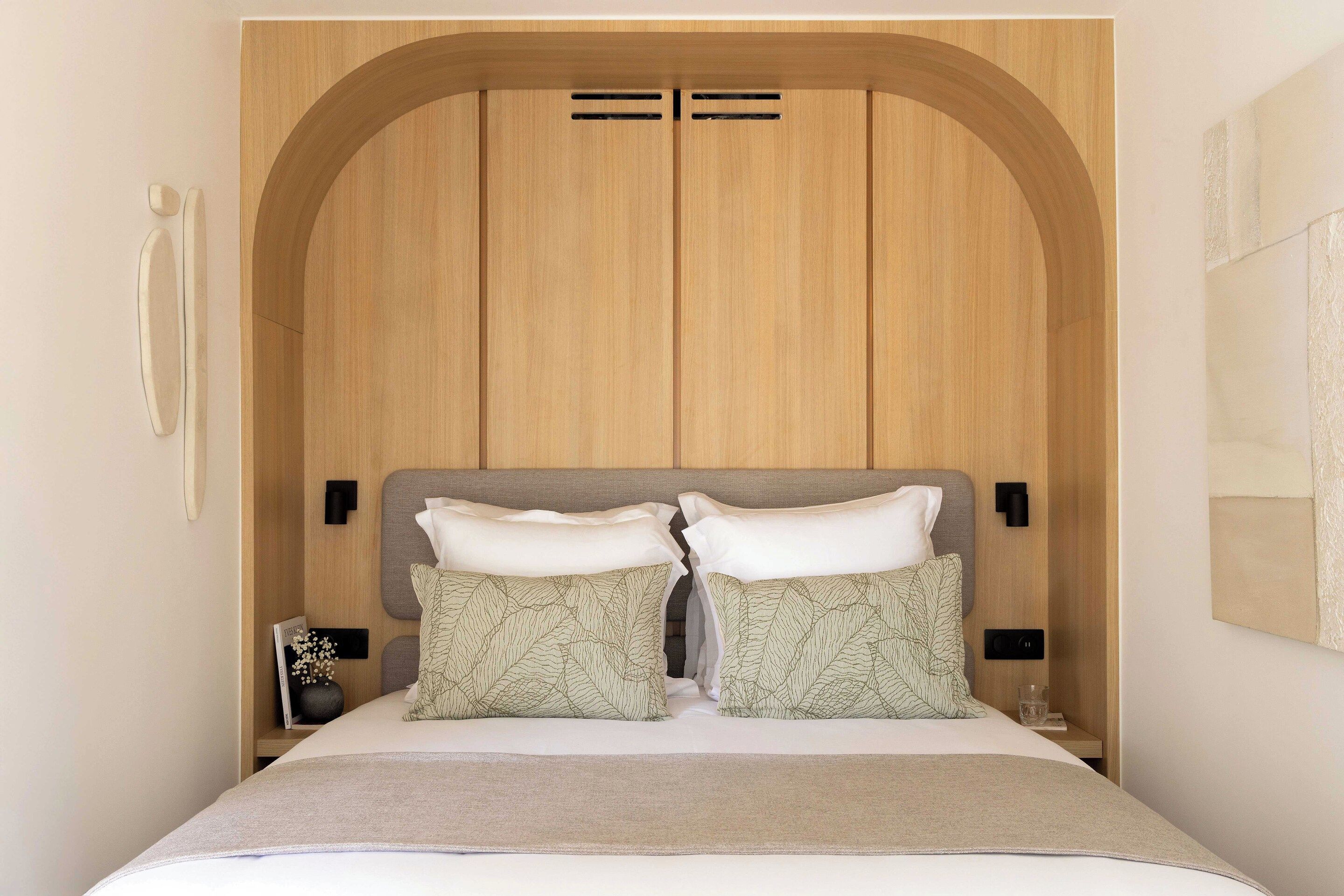 A bedroom with a wooden headboard, two bedside lamps, and a bed with a white comforter and patterned pillows.