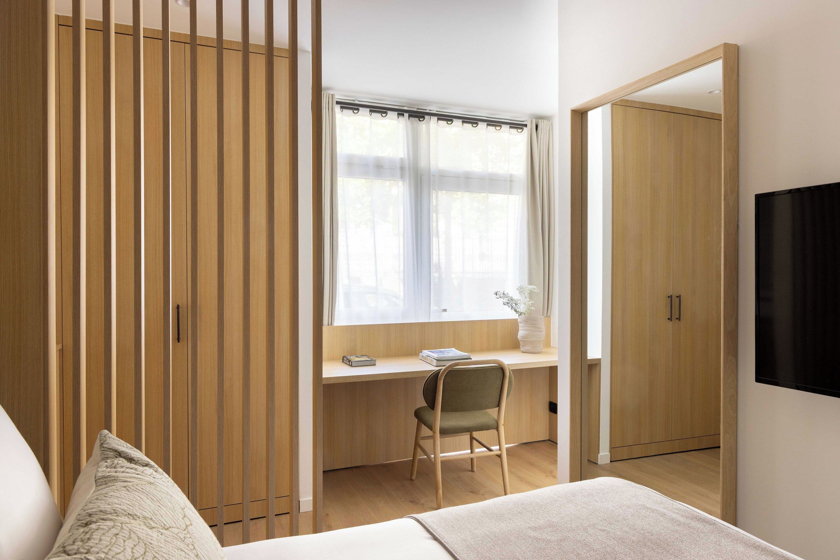 Un dormitorio con cama, escritorio, silla, ventana con cortinas y armario.
