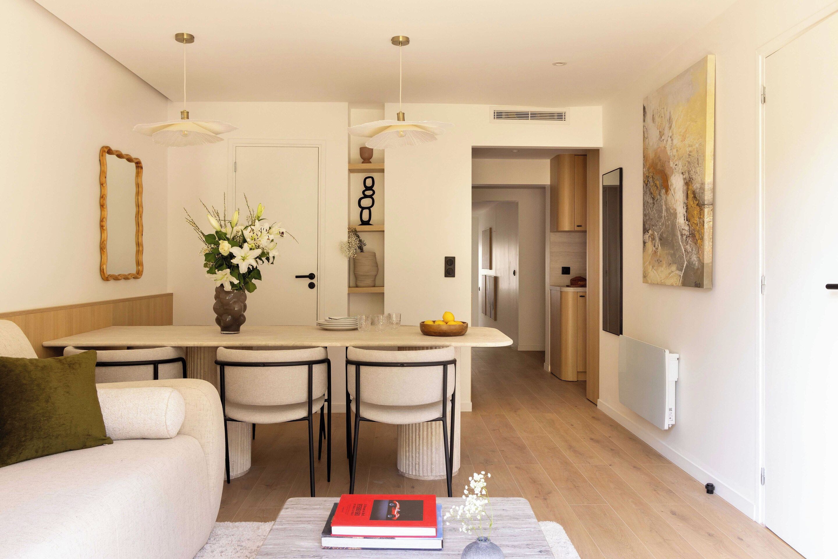 Una cocina moderna con una isla central, sillas de comedor, un sofá y una mesa de centro con libros.