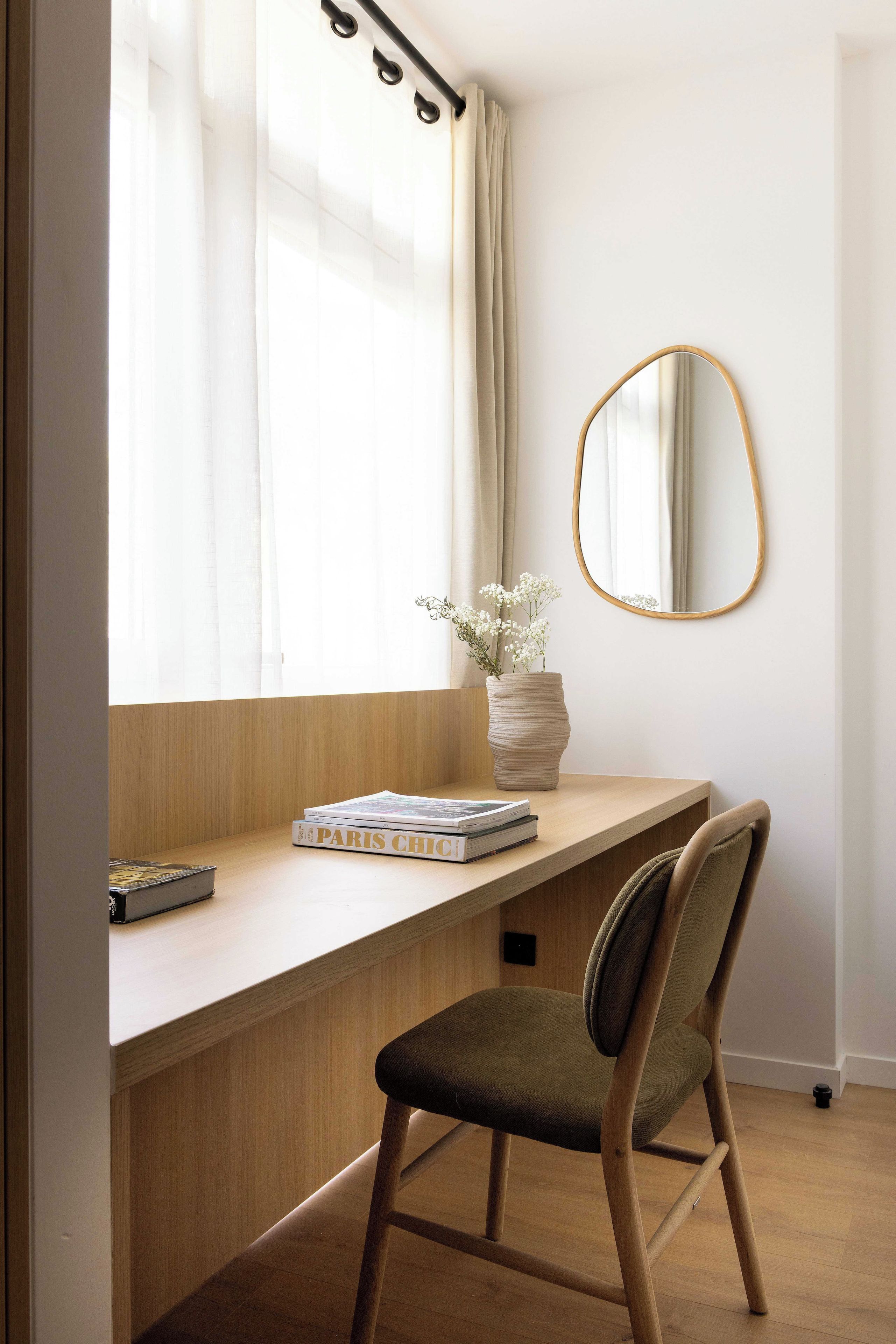 A study area with a wooden desk, a chair, a mirror, and a window with curtains.