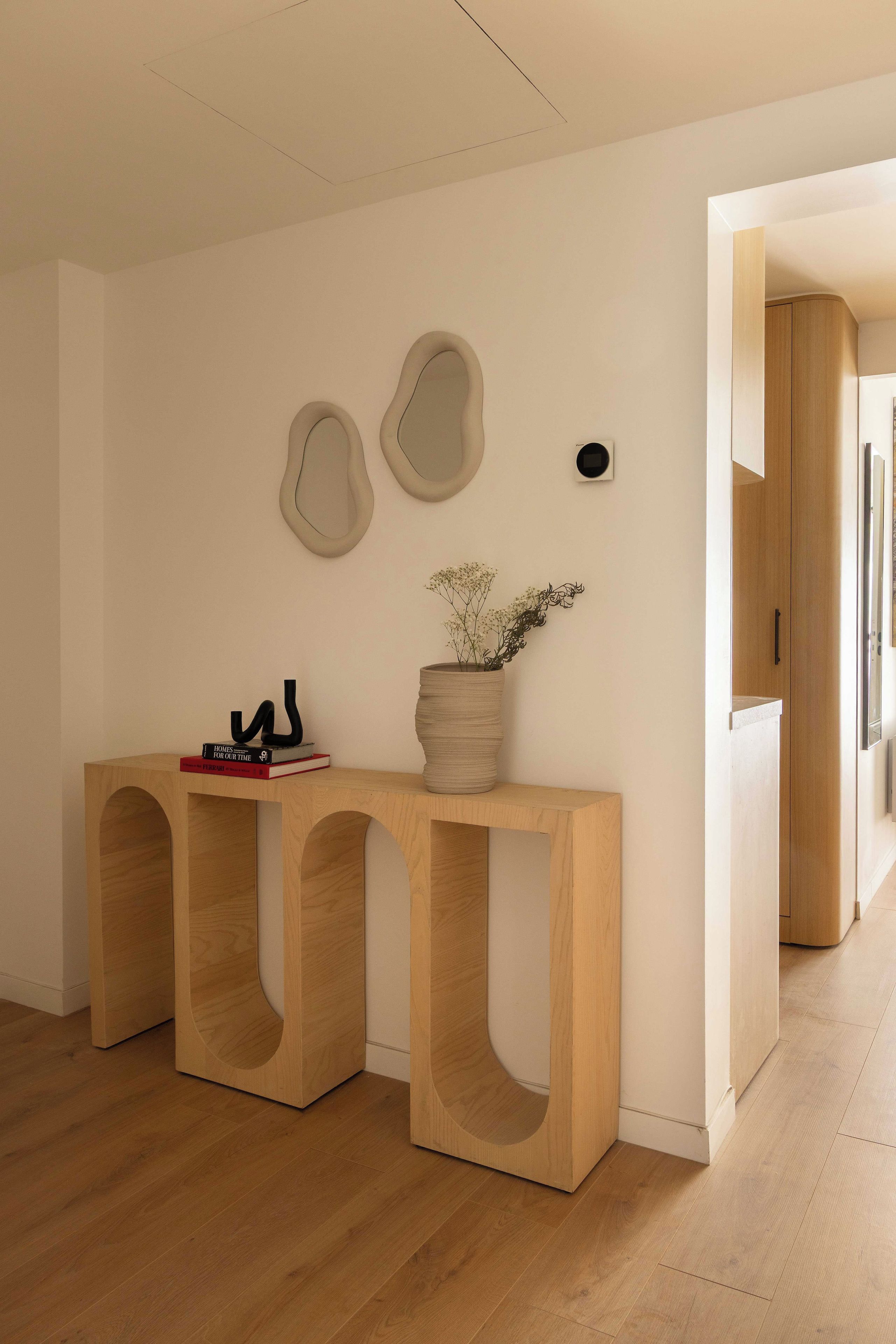 Un interior moderno con una consola de madera, un florero y arte en la pared.