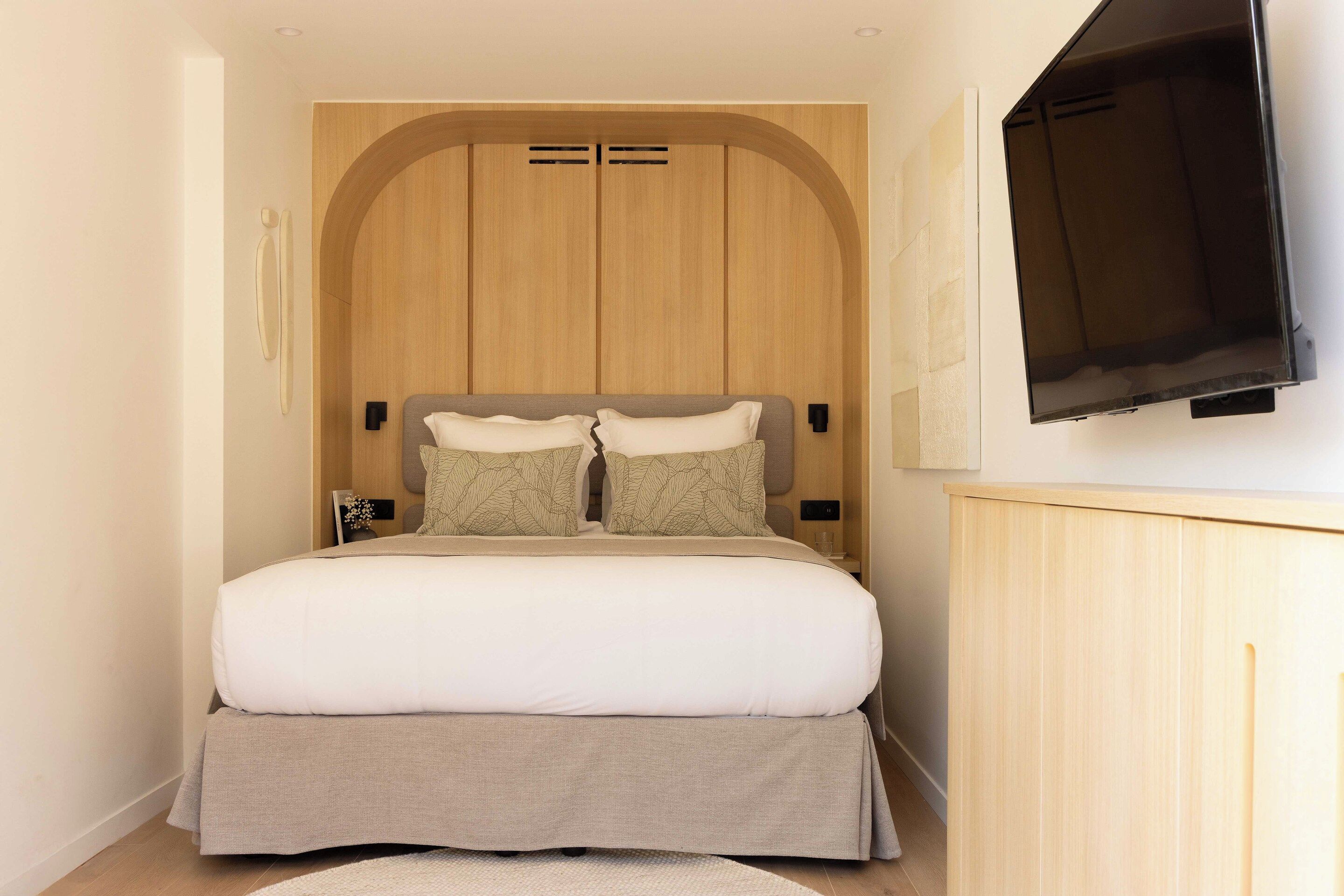Un dormitorio con cama, televisor montado en la pared y armario de madera.