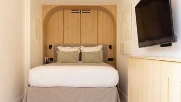 Quarto com cama, televisão na parede e guarda-roupa de madeira.