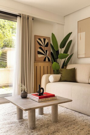 Uma sala de estar com sofá, mesa de centro com livros, planta e pintura na parede.