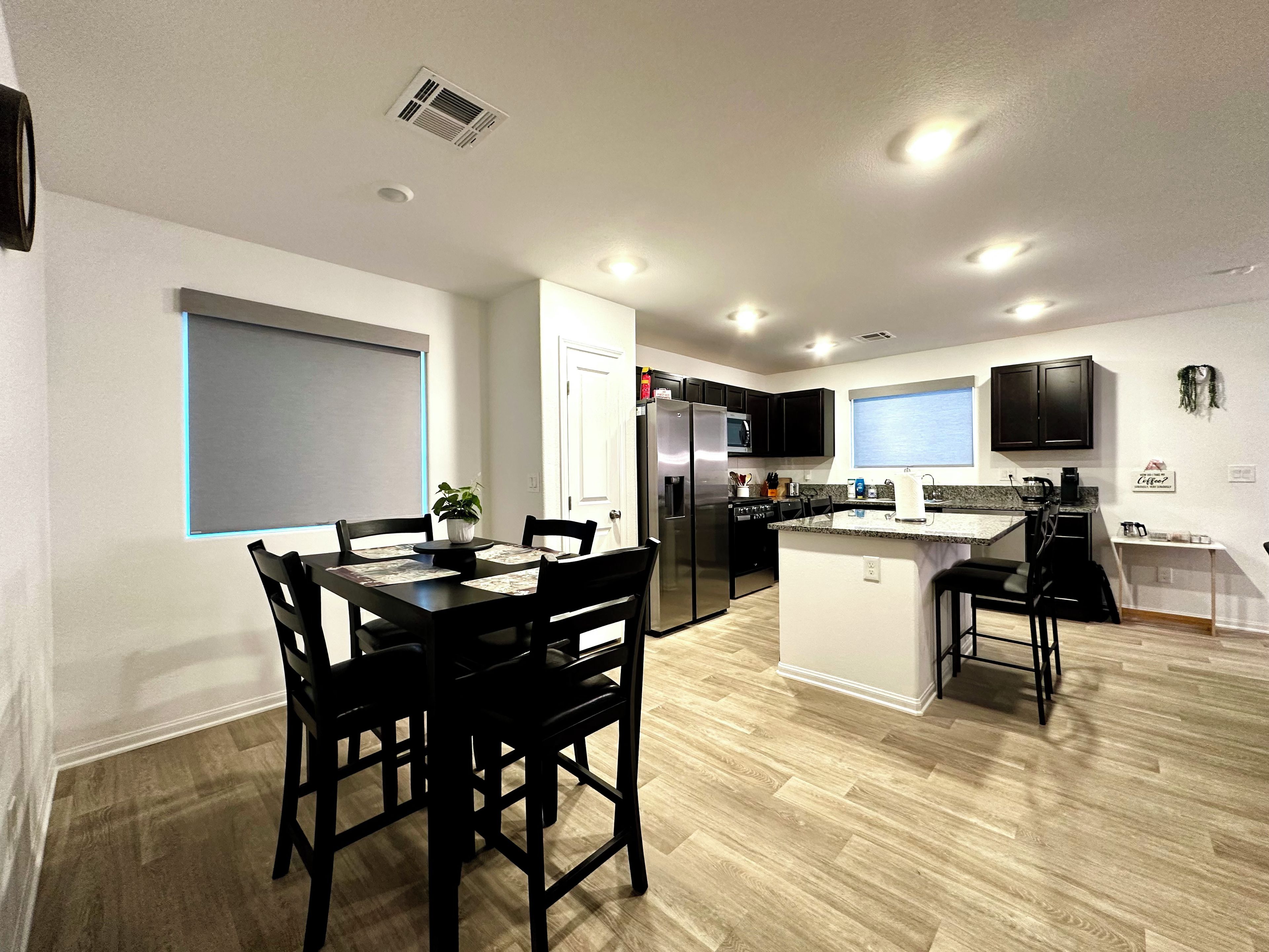 A modern kitchen with a dining area, featuring a central island, black cabinetry, and a window overlooking the room.