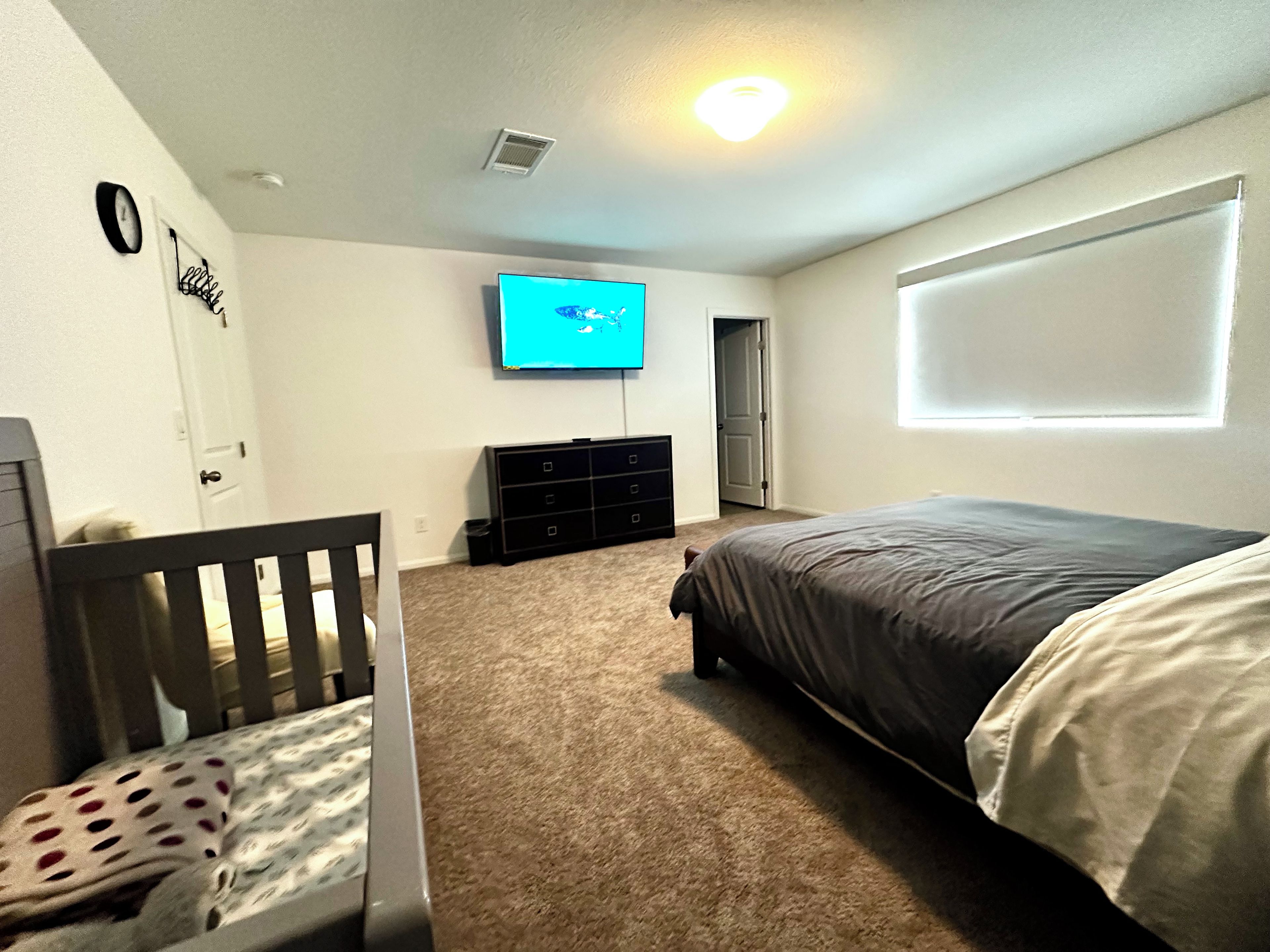 A bedroom with a bed, a dresser, a television, and a crib.