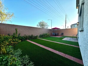 A backyard with a brick wall, green lawn, and a patio area with a table and chairs. - Spring Valley Villa (Las Vegas)