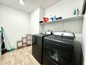 A laundry area with a washing machine and dryer, a mop, a vacuum cleaner, and a shelf with cleaning supplies. - Spring Valley Villa (Las Vegas)