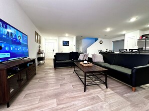 A modern living room with a flat-screen TV, a sofa, a coffee table, and a dining area with chairs. - Spring Valley Villa (Las Vegas)