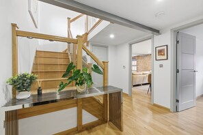 Un interior moderno con una escalera de madera, barandilla de vidrio y una planta en una consola.