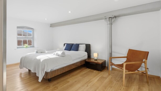 Ein modernes Schlafzimmer mit Bett, Nachttisch, Stuhl und einem Fenster.