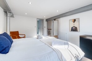 Un dormitorio moderno con una cama grande, una silla de madera, un armario y un cuadro en la pared.