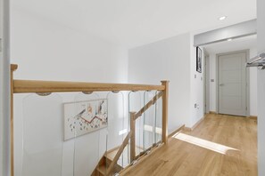 Una escalera con barandillas de madera y balaustradas de vidrio que conduce a una habitación con una puerta y un cuadro en la pared.