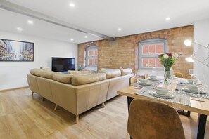 Una sala de estar moderna con un sofá color beige, una mesa de comedor lista para cuatro personas y una pared de ladrillo.