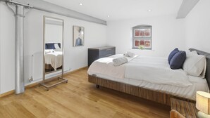 Ein modernes Schlafzimmer mit einem großen Bett, einem Kleiderschrank, einem Spiegel und einem Fenster mit Blick auf eine Ziegelwand.