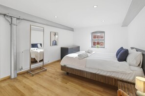 A modern bedroom with a large bed, a wardrobe, a mirror, and a window with a view of a brick wall. - The Cosy City Apartment of Lichfield (Lichfield)