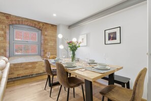A dining area with a brick wall, a window, and a table set for four with chairs. - The Cosy City Apartment of Lichfield (Lichfield)