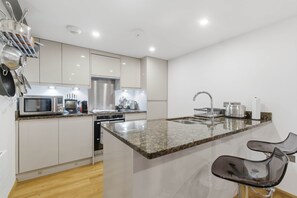 Una cocina moderna con electrodomésticos de acero inoxidable, encimera de granito y un taburete de bar.