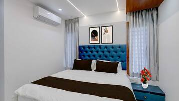 Un dormitorio con cama, cabecera, mesita de noche, un florero con flores y un aire acondicionado de pared.