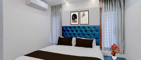 A bedroom with a bed, a headboard, a nightstand, a vase with flowers, and a wall-mounted air conditioner.