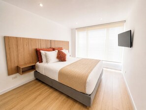 Ein modernes Schlafzimmer mit Bett, Holz-Kopfteil, eingebautem Regal und einem an der Wand montierten Fernseher.