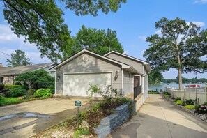 A single-story house with a garage, surrounded by greenery and a view of a lake. - Goguac Lake House|Sleeps6|Private Dock|Boat Launch (Battle Creek)