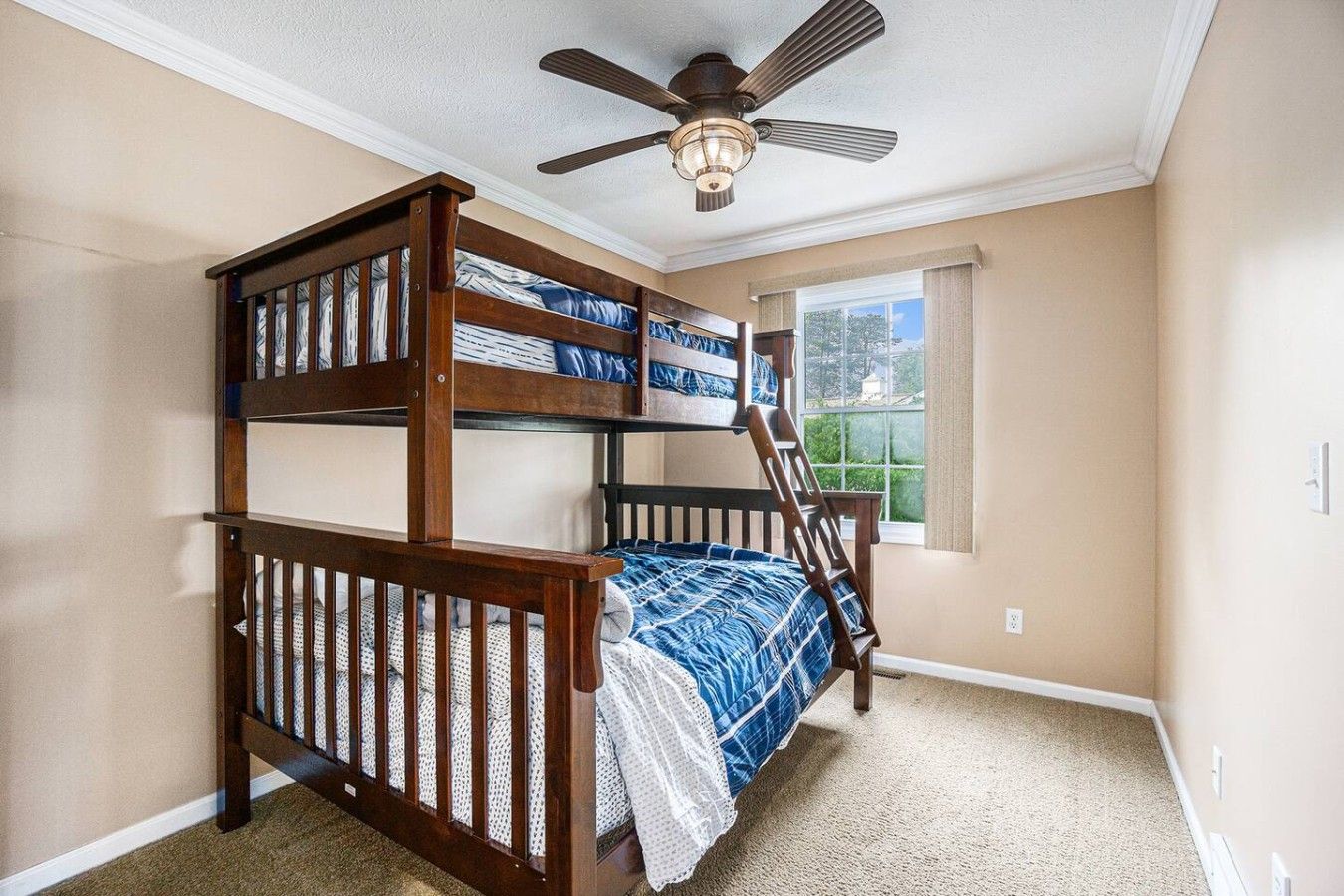 A bunk bed room with a ceiling fan, a window with curtains, and carpeted flooring.