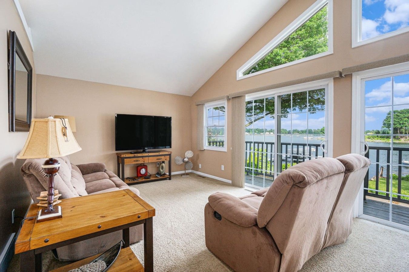 A spacious living room with a flat-screen TV, a wooden coffee table, a beige sofa, and a reclining chair.