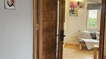 Een houten deur die leidt naar een kamer met een bed, een raam en een schilderij aan de muur.